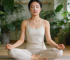 Woman meditating with nasal strips for improved breathing in a lush plant-filled room.