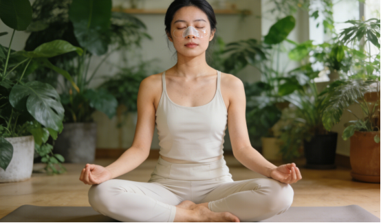Woman meditating with nasal strips for improved breathing in a lush plant-filled room.