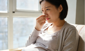 Pregnant woman pinching her nose, suffering congestion, considering nasal strips for relief.