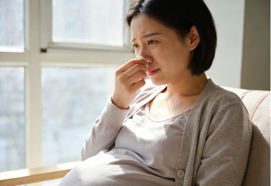 Pregnant woman pinching her nose, suffering congestion, considering nasal strips for relief.