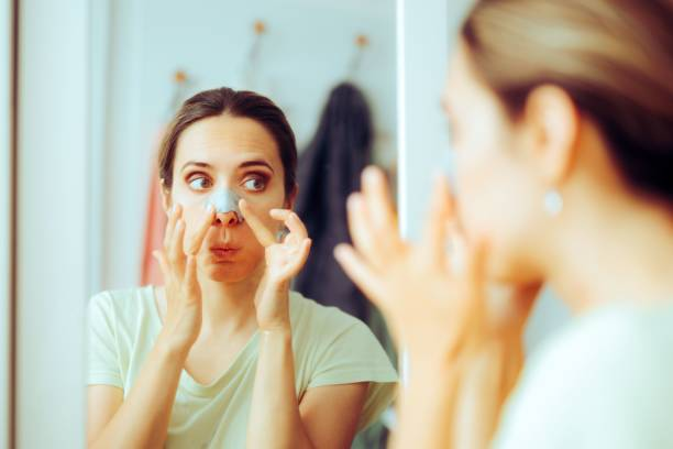 Woman applying a black pore cleansing nasal strip in the mirror.
