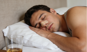 Man sleeping peacefully with nasal strips applied for better breathing, a drink on nightstand.