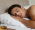 Man sleeping peacefully with nasal strips applied for better breathing, a drink on nightstand.