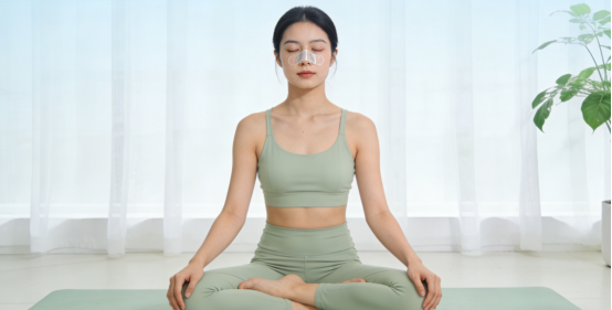 Serene woman in lotus pose wearing nasal strips, enhancing breath during meditation.