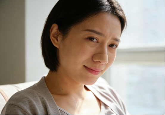 Pregnant woman smiling subtly with a nasal strip applied, breathing easier.