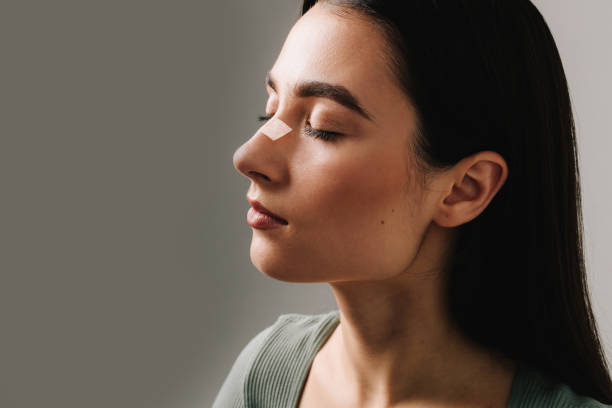 Young woman in profile wearing a clear nasal strip on her nose for better breathing.