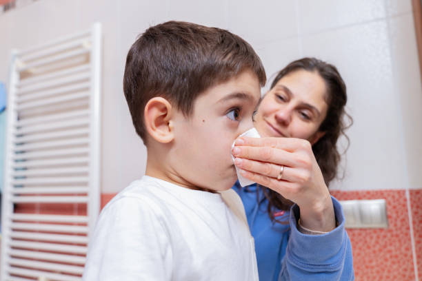 An adult carefully applying a small white nasal strip to a child's nose.