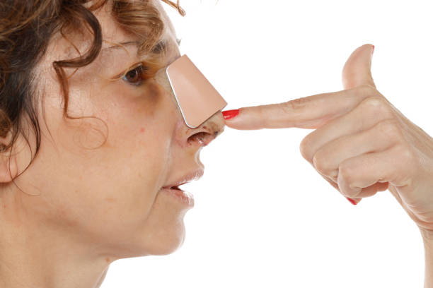 Woman with a beige nasal strips applied to her nose, someone pointing.
